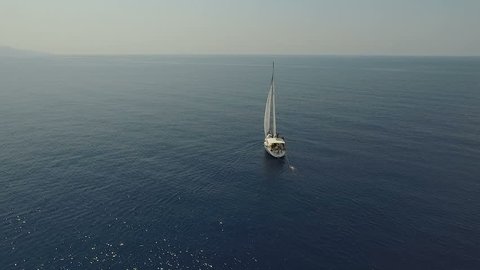 Sweeping aerial shot of large sailboat off beautiful coastline