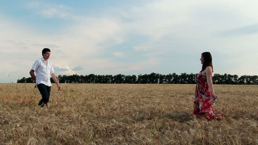 Young couple holding hands and walking through wheat field.