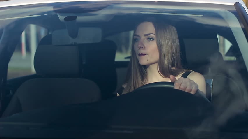 A young woman is using lipstick in a car