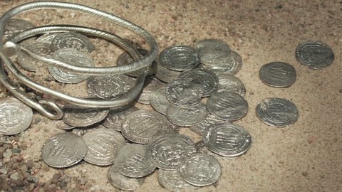 Silver dirhams and spiral from Viking age on sand. The silver dirham seems to have been the standard coin for Viking trading practices