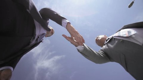 Businessmen of different age viewed from below shaking hands and talking