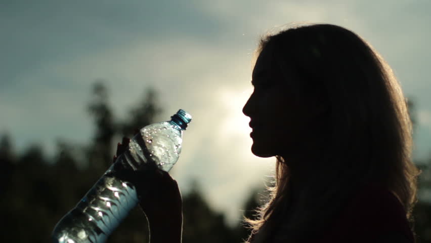 Silhouette of sporty young woman drinking mineral water after fitness 