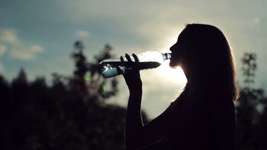 Silhouette of young woman drinking water over sunset 