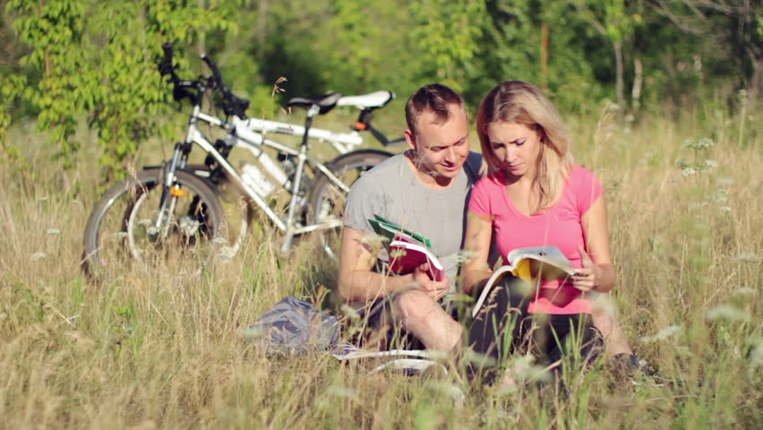Pair of attractive students looking at the books in the park 