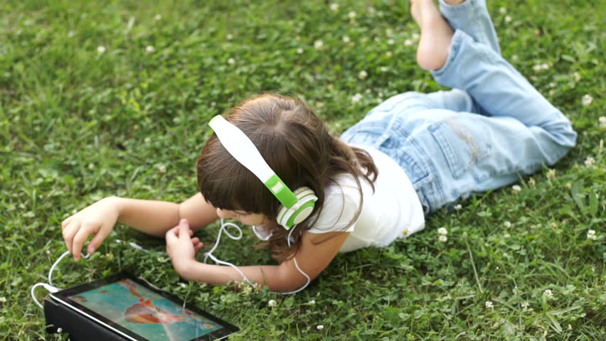 Girl in headphones drawing with a finger in the tablet pc outdoors
