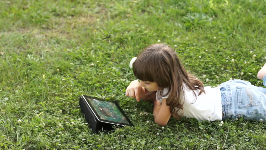 Girl playing with tablet pc lying on the grass
