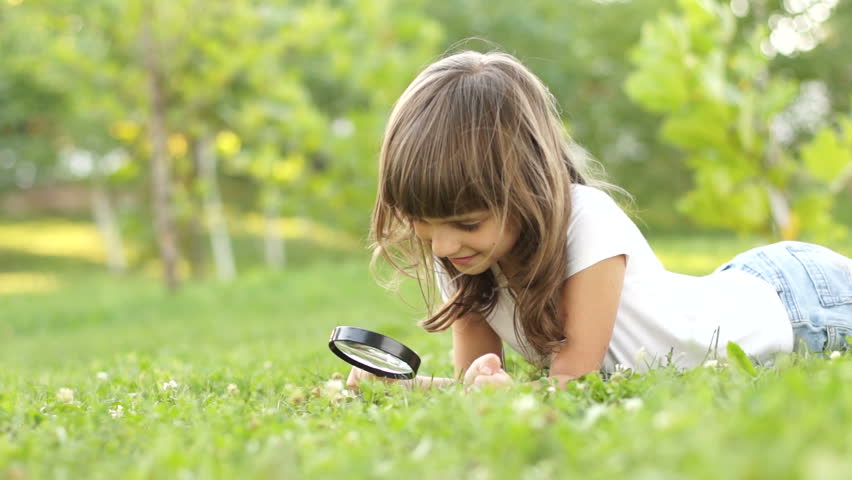 Girl with magnifier lying on the grass
