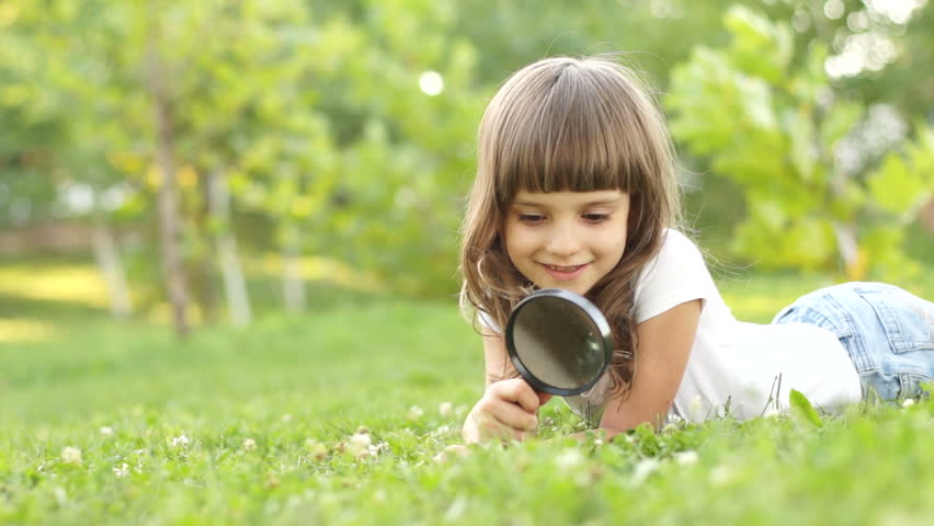 Girl with magnifying glass lying in the grass
