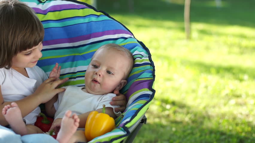 Newborn baby and his sister sitting in a chair outdoors with vegetables
