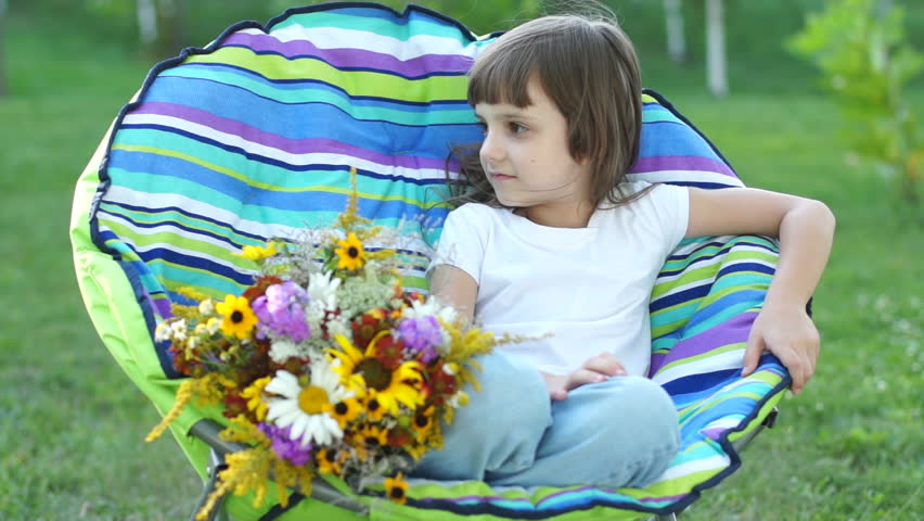 Girl with flowers sitting in a chair outdoors and looking at camera
