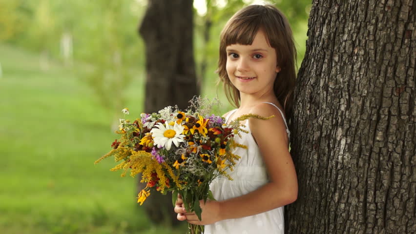 Smiling girl with bouquet of flowers near the tree
