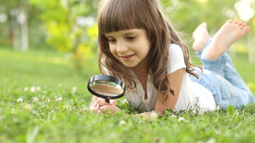Portrait child with magnifier lying on the grass
