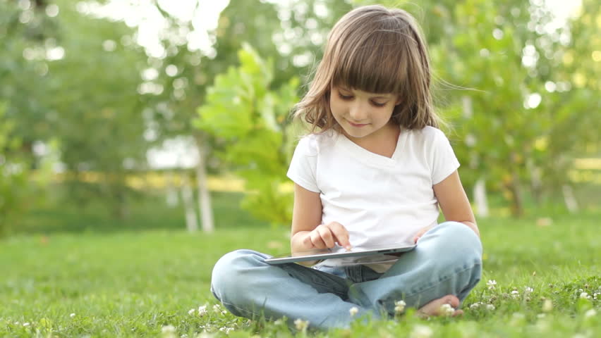 Little girl with a tablet pc sitting on the grass
