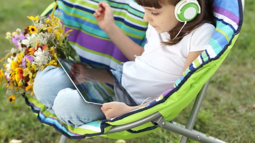 Girl in headphones listening  music from Tablet PC outdoors

