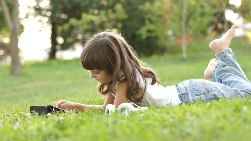 Girl with a tablet pc lying on the grass and looking at camera
