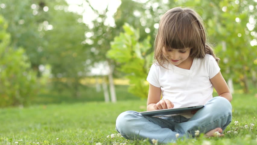 Little girl with a tablet pc thumbs up. Ok. Sitting on the grass outdoors
