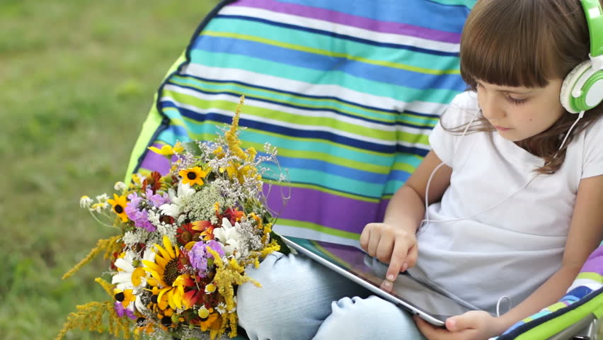 Girl drawing in a Tablet PC, and sitting in a chair outdoors
