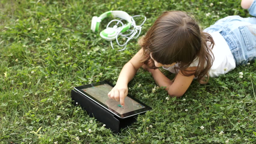 Drawing a girl with a finger in the tablet pc lying on the grass

