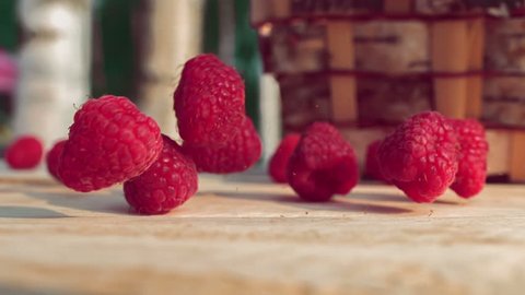 Raspberries fall on a wooden table next to a wicker basket. Berries crumble on the table. Slow shooting