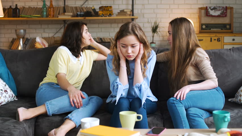 young girl is unhappy, sad and depressed because her bad female friends offend her, conflict and pressure discussing behind the back, while sitting on sofa at home during sunny day Royalty-Free Stock Footage #25918955