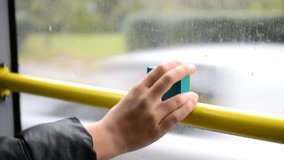 Hand of a teenager or child holding an action camera near a window in a moving bus to film what is going on outside.