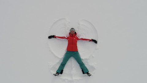 Top view of snow angel. Camera moves out from woman lying in snow and making snow angel
