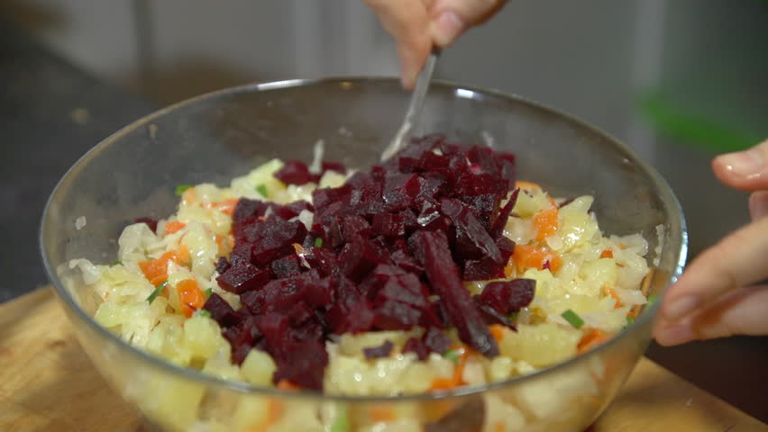 Female hands mixing rustic vegetable salad of beets,potatoes, carrots, cabbage, green onion on the wooden background, shoot close up.