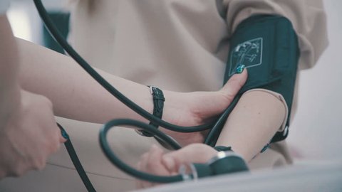 Doctor and patient blood pressure check up - Female patient's arm extended. Doctor checking blood pressure of a patient, he is measuring heart pulses with a sphygmomanometer