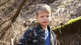 Closeup portrait of lonely unhappy adorable blond kid looking at camera first, then child becomes angry and closes his face with hand from camera. Real time full hd video footage.