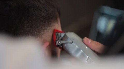 Barber makes a male haircut with a professional hair trimmer in a barbershop, close-up.