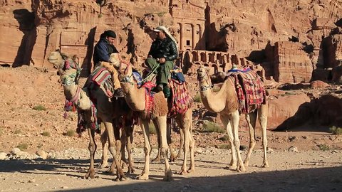 JORDAN, PETRA, DECEMBER 5, 2016: Jordanians on camels near Royal Tombs in Petra, originally known to Nabateans as Raqmu - historical and archaeological city in Jordan. Silk and Urn Tombs on background