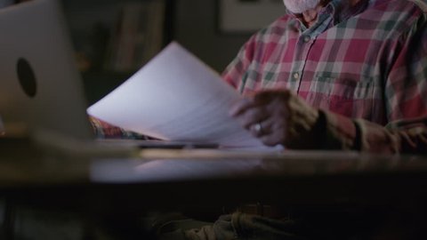 Close up of frustrated older man with paperwork and laptop at night / Cedar Hills, Utah, United States