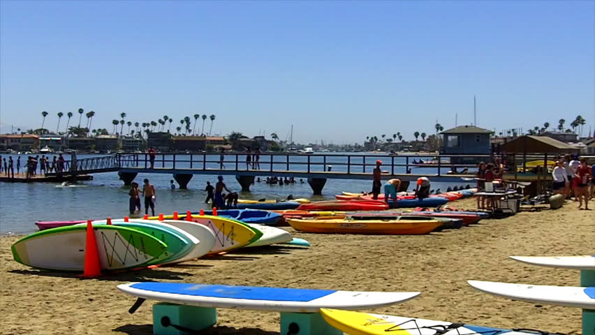 Kayaks and paddle boards are seen in the foreground and swimmers on a dock in