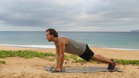 Dumbbell Plank Row. Fitness man doing Alternating Renegade Row exercise using dumbbells while exercising outside on beach. SLOW MOTION video.