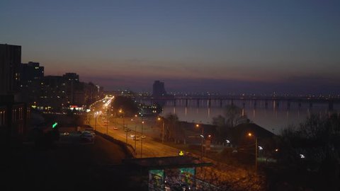 Dnepropetrovsk/ukraine - Mar 21 2017: Riding Cars Along the Embankment and Bridge, Walking Pedestrians on the Background of Houses, the Setting Sun and the River,the Car Arrived at the Gas Station