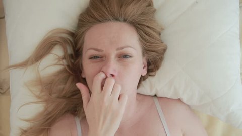 The woman lies on the bed and picks her finger in the nose, close-up. view from above