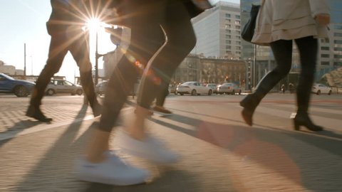 Young Lady in a coat and white sneakers is crossing the road with People from the Crowd at a Pedestrian Crossing in Sunny Weather