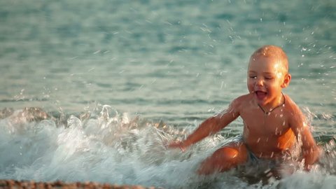 Happy kid splashing in the surf on a summer beach: stockvideo