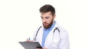 Serious surprised young male doctor listening and writing to folder information isolated