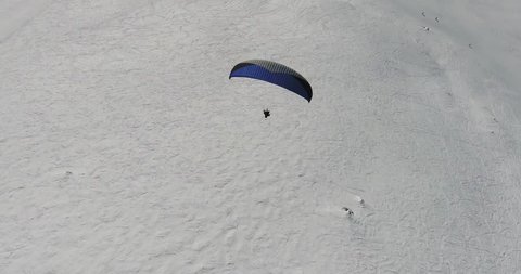 Paragliding sport in winter season. Parachute sky-diver flying over high mountains with fresh snow on sunny winter day. Top aerial  view. Caucasus Mountains, Georgia, ski resort Gudauri. 