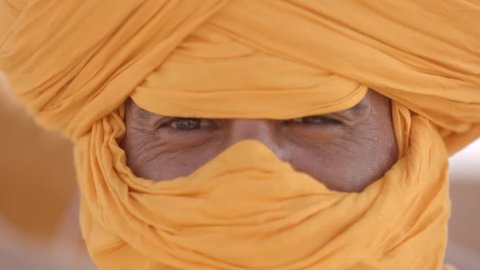 Portrait shot of a Arab male traditional looking serious into the camera. The male lives as nomad in the desert. 