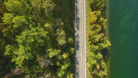 Car rides on the road between trees near the lake. green Forest. Sunny summer spring day. Green water. Mountains. Top view of cars. Aerial view top down 4k