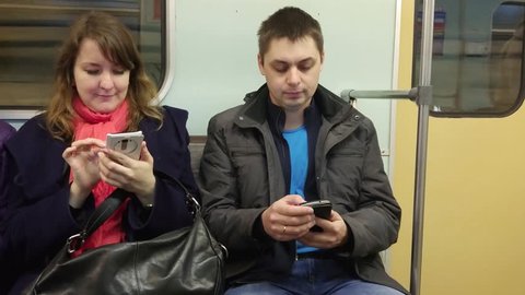 Man and woman sit and watch in smartphone in hands in wagon of metro train, mobile phone video.