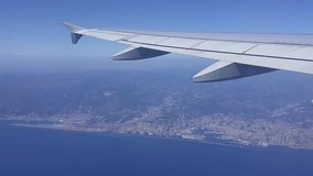 View from fly airplane to sky, wing above blue sea and shore of Genoa, mobile phone video.