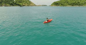 Video from drone. Beautiful young girl floating on a kayak in a beautiful bay on a sunny day. The girl crosses the bay using the kayak. Nai Harn beach, Thailand 2017.
