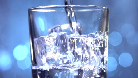 Water is pouring into a glass with ice cubes. Clear water pours ice cubes on a blue flickering background. Pure water  with Ice and bubbles in glass.