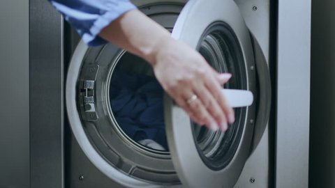 Loading washing machine. Load clothes to washer machine. Female hand put uniform in laundry machine. Load clothes laundry washing machine. Preparing laundry washing