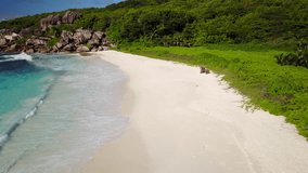 4k aerial video flying over empty wide sand beach with waves and granite rocks of tropical seychelles island
