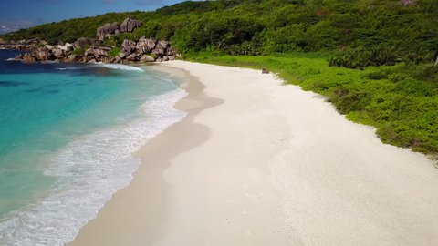 4k aerial video flying over empty wide sand beach with waves and granite rocks of tropical seychelles island
