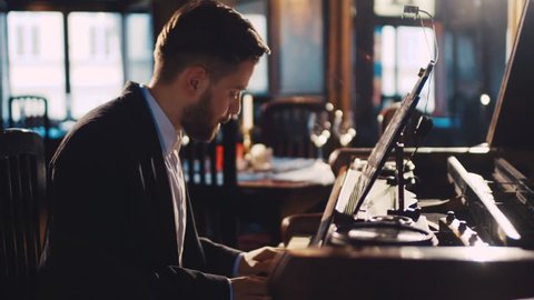 Close up view of an old-fashioned bearded pianist playing the fortepiano in a deserted restaurant. Enjoying the music, jazz. Elegant outfit. Romantic atmosphere.